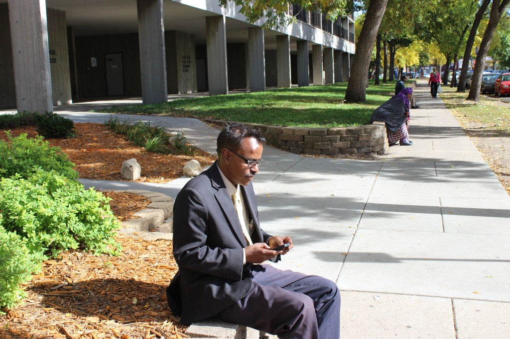 Abdirizak Bihi checks his email and text messages outside Riverside Plaza. Photo: Aiden Pink / The Tower