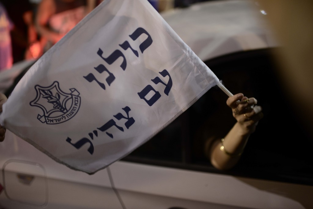 A woman holds a flag reading "All of us are with the IDF: as she drives by a demonstration in Rabin Square in Tel Aviv, July 26, 2014. Photo: Tomer Neuberg / Flash90