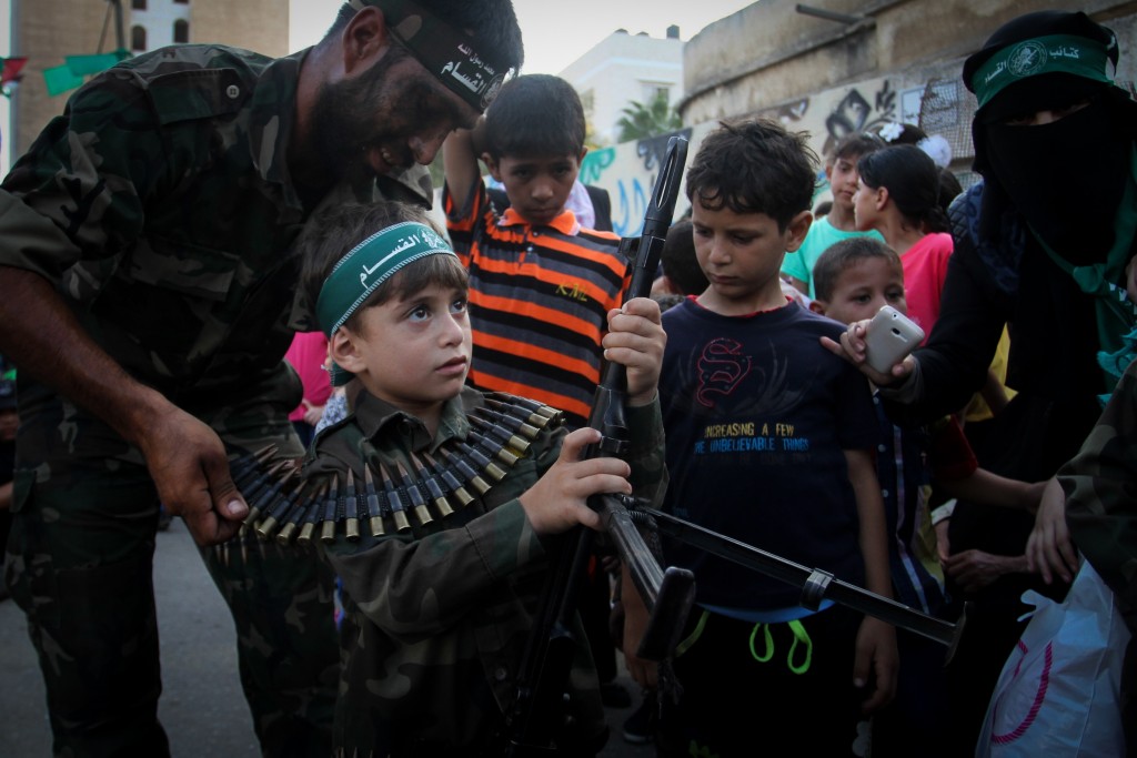 A Palestinian boy holds his father's weapon during a graduation ceremony as part of a military-style summer camp organized by Hamas, August 2015. Photo: Abed Rahim Khatib / Flash90